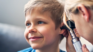 Doctor using otoscope to examine the young, smiling boy's ear.