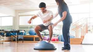 Male athletic patient standing on balance ball