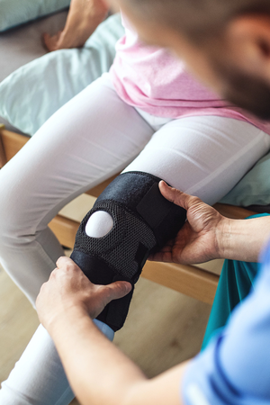 Doctor putting a knee orthosis on a woman patient