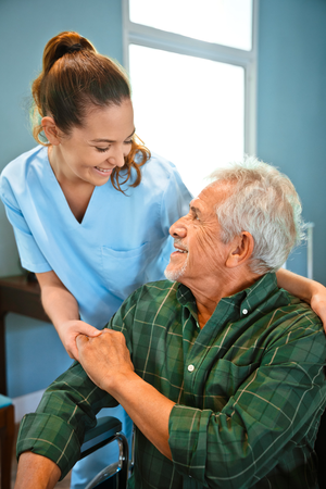 Smiling nurse holding hands of man in wheelchair