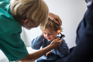 Female doctor examining boy's ear with otoscope in hospital.