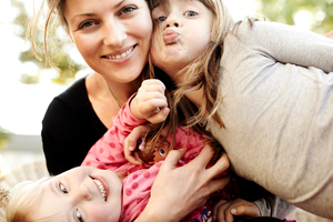 Mother holding two young daughters and smiling.