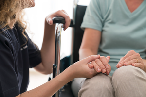 Young home nurse holding hands of senior woman in wheelchair.