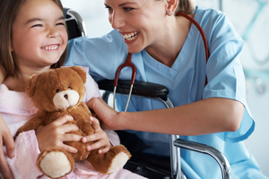 A nurse laughing with a little girl in her wheelchair at the hospital